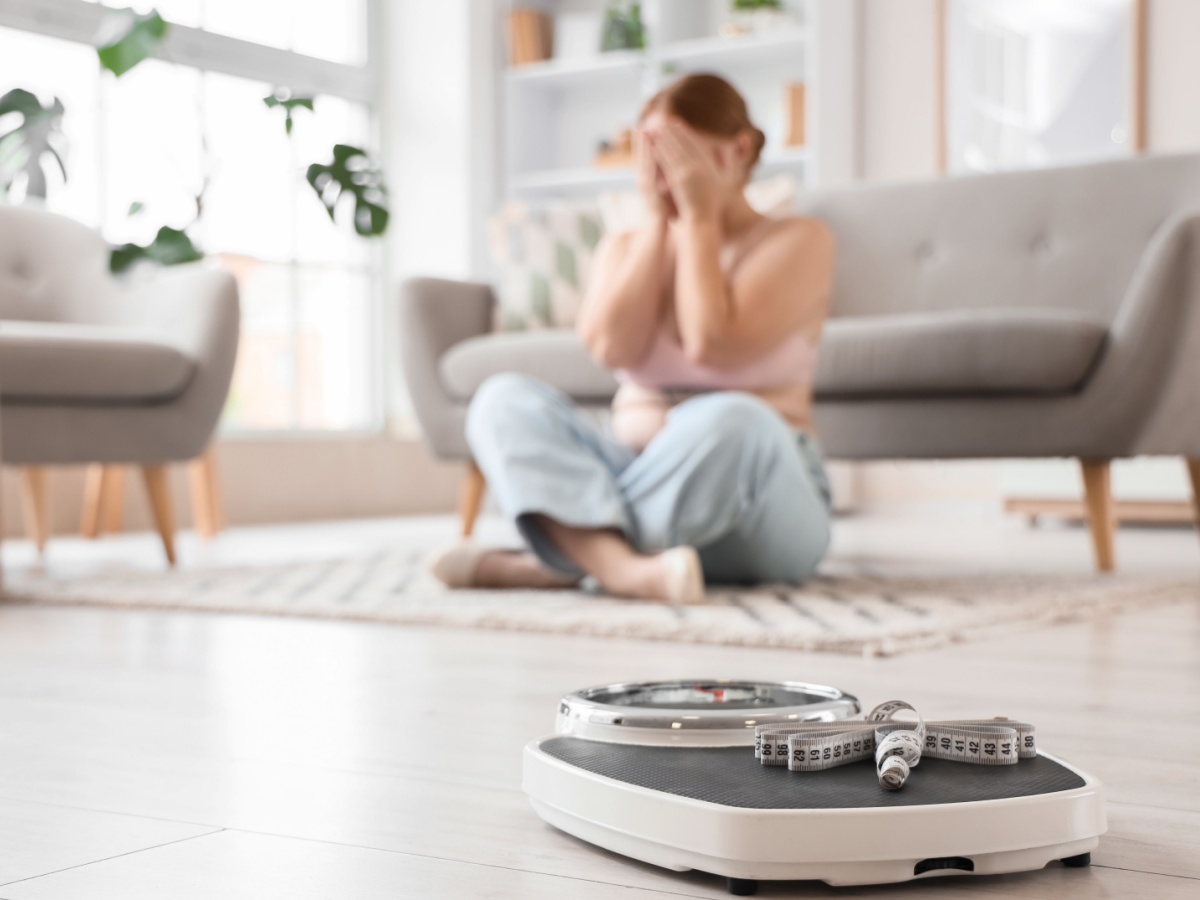 Weight scales with tape measure against upset overweight woman at home, closeup